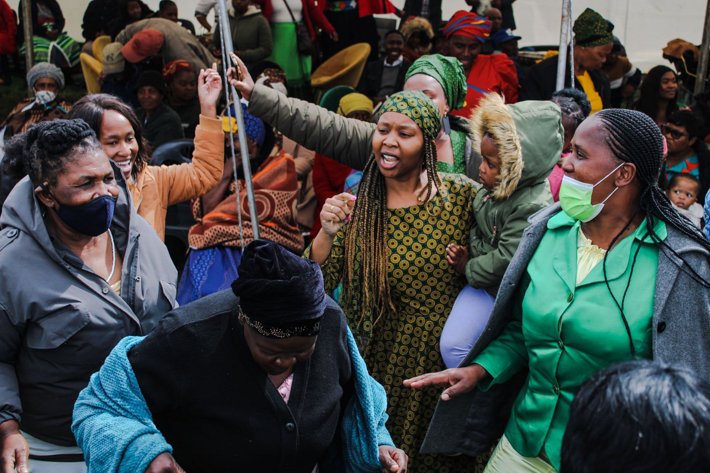 Women and children gathered under a tent at a lively South African community meeting.